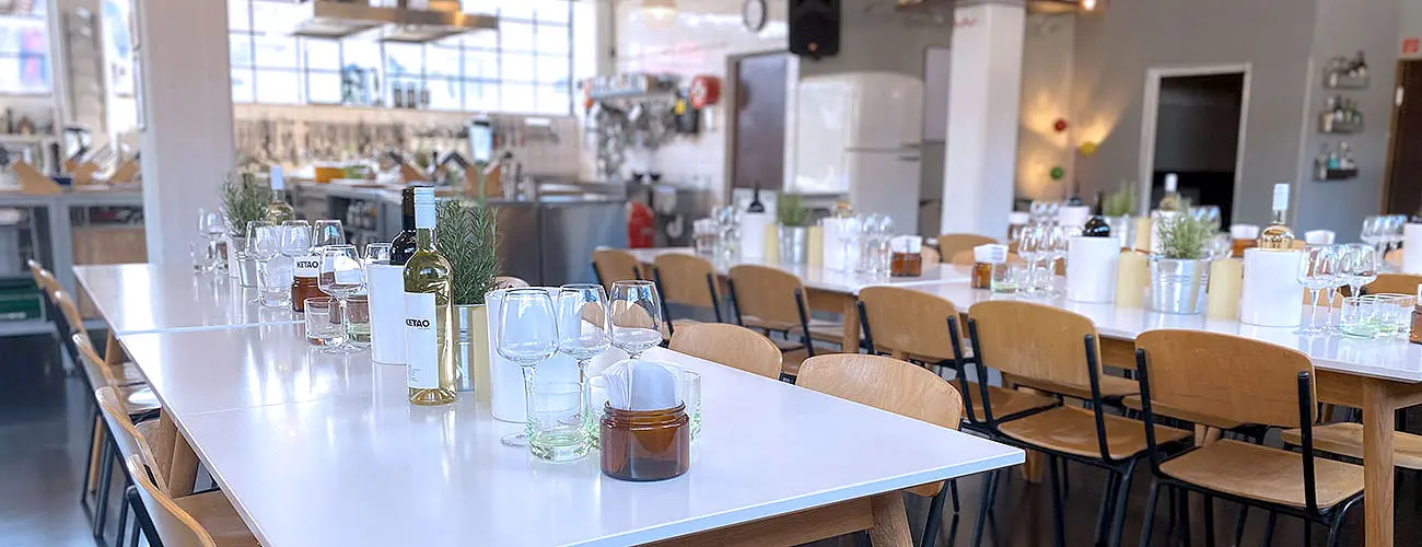 Helle Location mit langen Tafeln und Blick auf die Küche