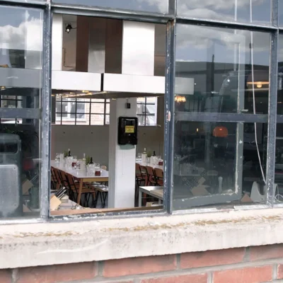 blick-durch-industriefenster-gastraum-gedeckte-tische Blick durch Industriefenster in modern eingerichteten Gastraum mit gedeckten Tischen und Flaschen auf den Tischen