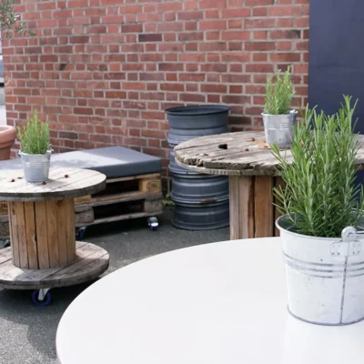 aussenbereich-holztische-kraeutertoepfe-backsteinwand Gemütlicher Außenbereich mit Holztischen aus Kabeltrommeln und Kräutertöpfen vor roter Backsteinwand