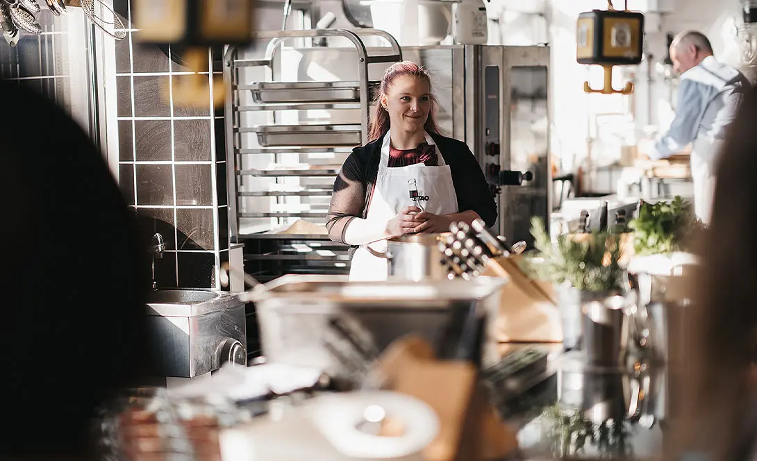 Köchin mit Schürze steht in moderner Profiküche und lächelt