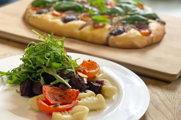 gnocchi-mit-rinderfilet-und-pizza Hausgemachte Gnocchi mit Rinderfilet, Rucola und Ofentomaten, im Hintergrund Pizza