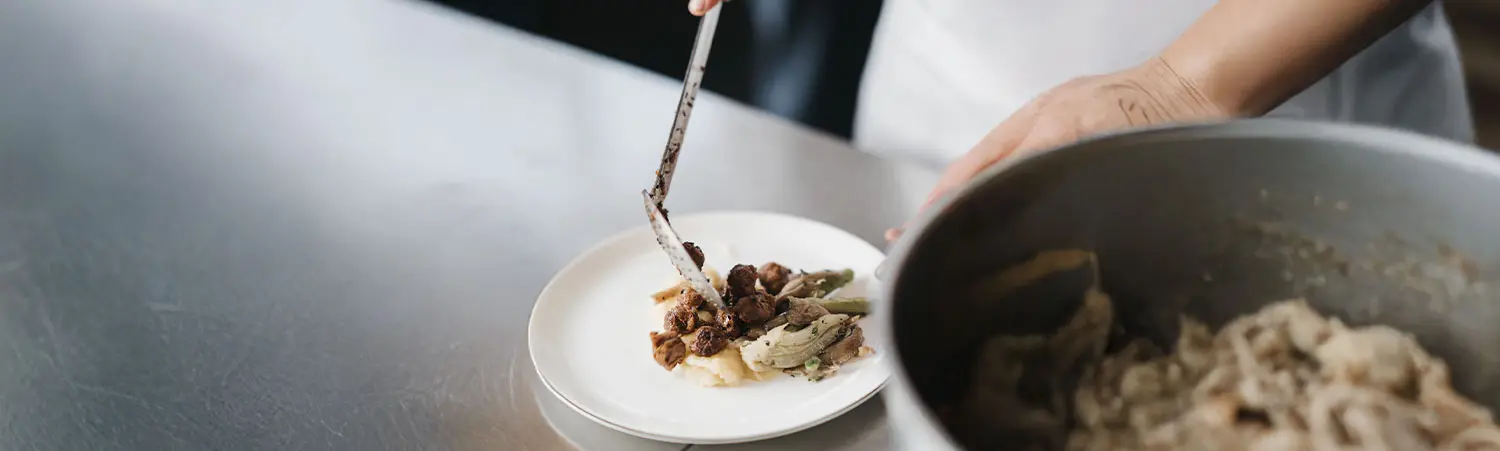 Zubereitung eines Hauptgangs – Portionieren von Speisen auf weißem Teller