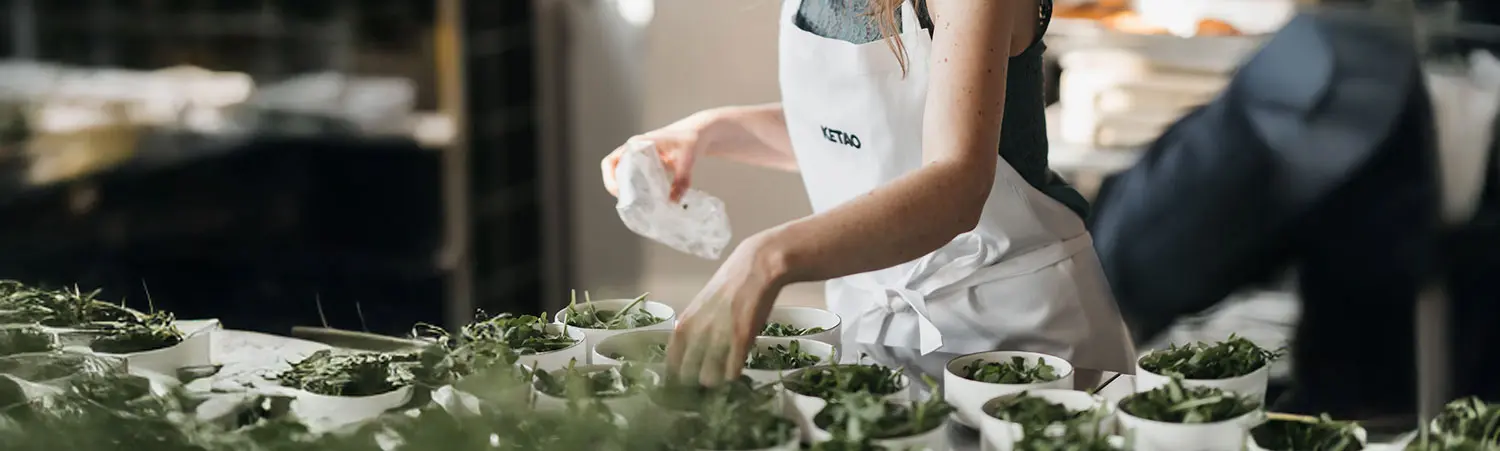 Vorbereitung von mehreren Schalen mit grünem Salat in Profiküche