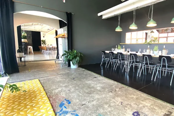 Eventlocation mit langen gedeckten Tischen, schwarzen Wänden und buntem Betonboden