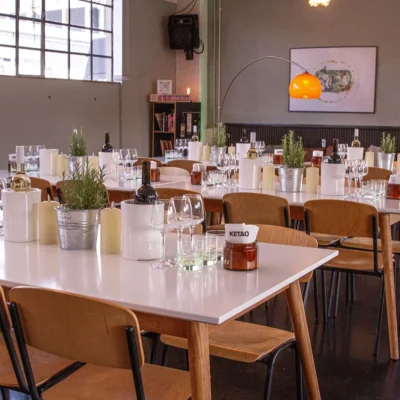 dinner-eventraum-ketao Eingedeckte Tische mit Wein, Gläsern und Kräuterdeko im modernen Eventraum