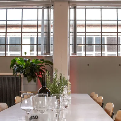 tisch-industriefenster-wein Festlich gedeckter Tisch mit Wein und Pflanzen vor großen Industriefenstern