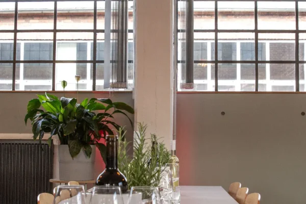 Festlich gedeckter Tisch mit Wein und Pflanzen vor großen Industriefenstern