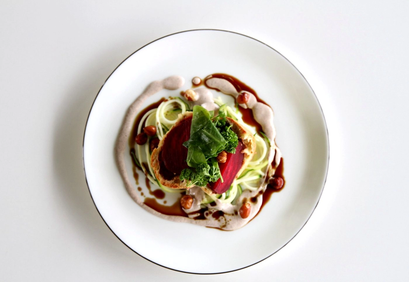IMG_8903_web - KETAO | FRISCH. LECKER. ANDERS. Plate with rare beef slices atop spiralized vegetables, garnished with greens and brown sauce around the edge on a white plate.