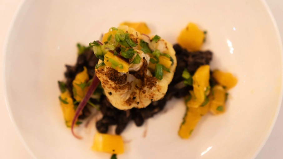 Bildschirmfoto 2026-10-01 um 10 - KETAO | FRISCH. LECKER. ANDERS. Plate of roasted cauliflower resting on black beans, with mango salsa, corn kernels, and fresh herbs on a white plate.